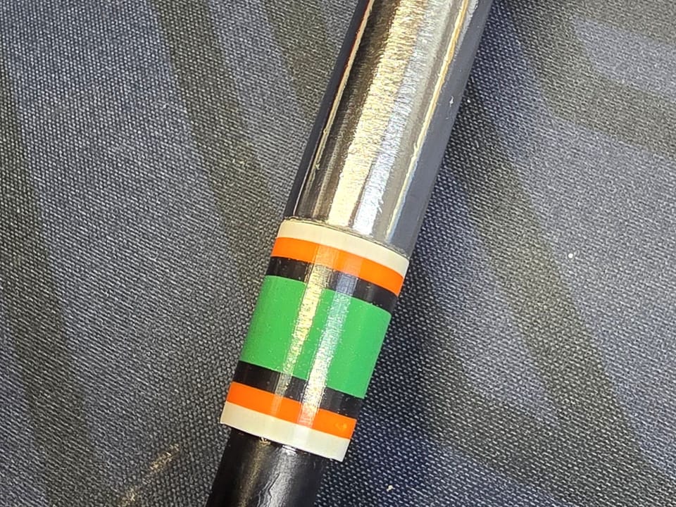Close-up of a custom 3D-printed ferrule with orange, white, black and green stripes on a chrome hosel