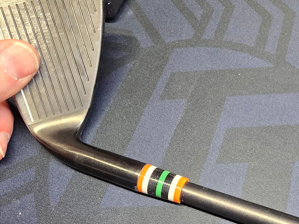 A striped custom ferrule on a black-shafted wedge, face up on the bench mat